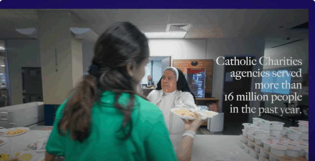 A nun hands a plate of food to a young woman with long brown hair. The photo is a screenshot from a video and displays the text, "Catholic Charities agencies served more than 16 million people in the past year"